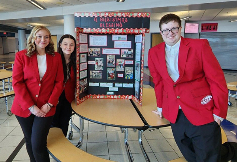 Three early childhood education students (one male, two females) stand my display board at FCCLA competition