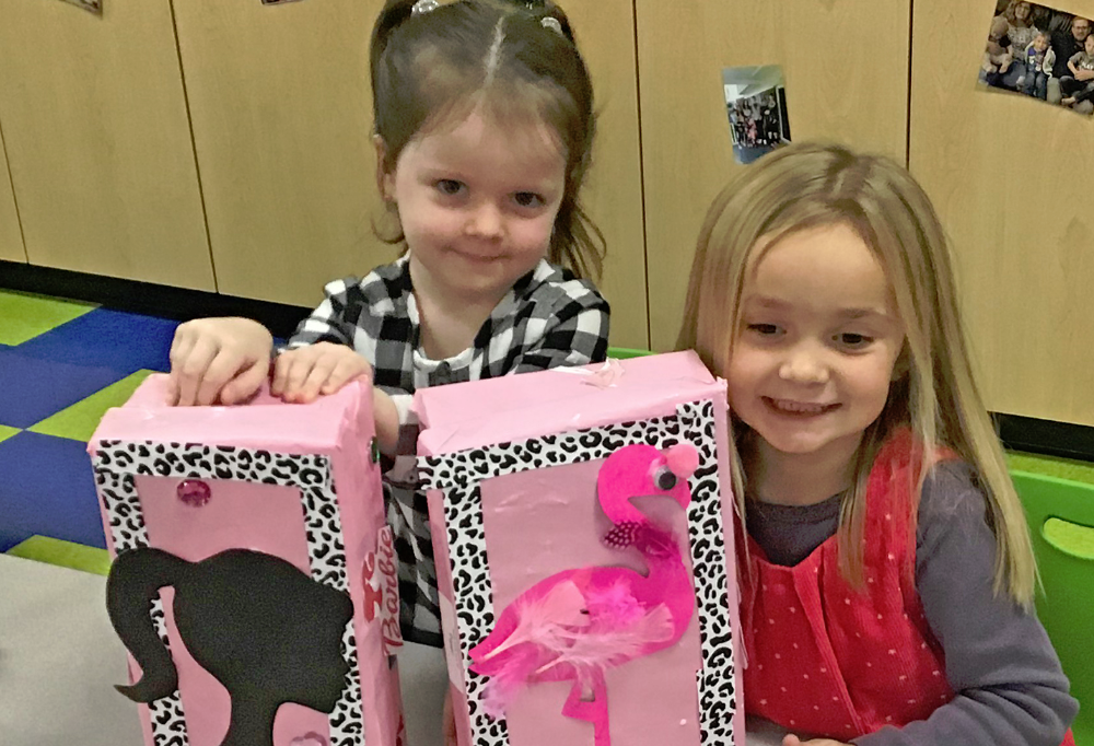Two female preschoolers smile with their shoeboxes filled with gifts
