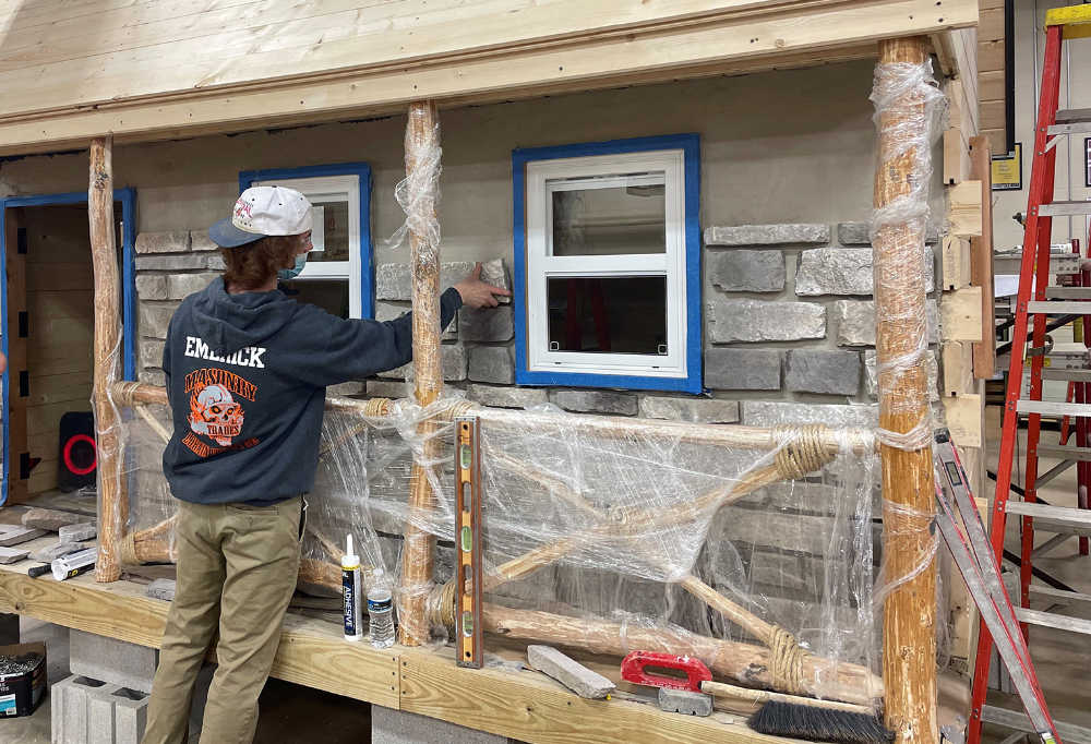 Senior Masonry Trades student Andrew Emerick (Keystone) applies the stone to the front of the playhouse 