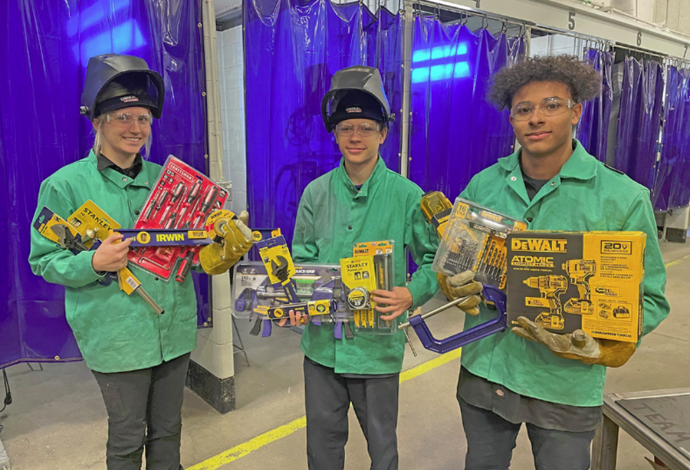 One female and two male welding students smile while holding donated tools in their welding lab.